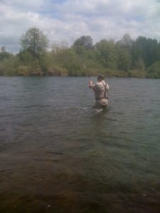 Fly fisherman standing in the Mckenzie River in Oregon fighting a large Rainbow trout he hooked on a Possie Bugger fly. Getting a good "dead drift" is one of the keys to hooking fish like this one.